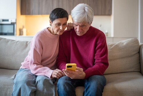 elderly couple seated on sofa together reviewing smartphone with concerned expressions