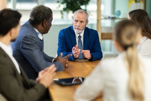 senior attorney in suit gesturing during professional group meeting at conference table