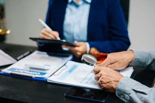 person using magnifying glass to review contract documents on desk