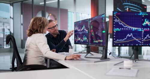 two brokers reviewing live stock market charts on multiple trading monitors