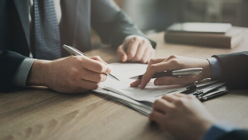 two professionals signing agreement document on wooden office desk