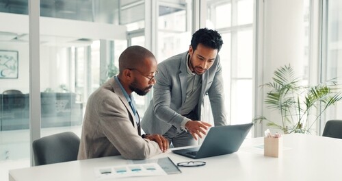two professionals in suits collaborating over laptop at office conference table